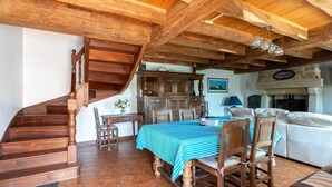 Eine Holztreppe führt zu einem Essbereich mit einem Tisch für vier Personen, einem weißen Sofa und einem Kamin aus Stein.