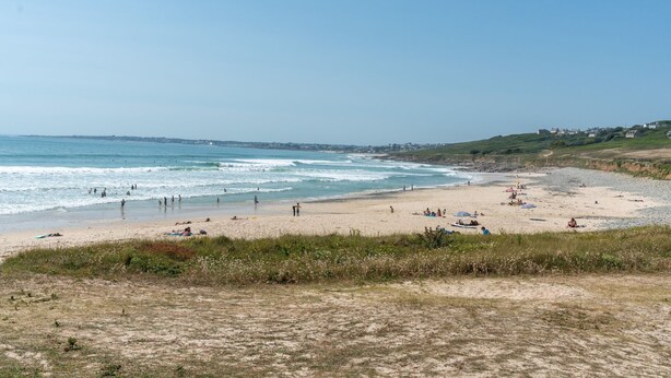 Ein Strand mit Menschen, einem klaren Himmel und Häusern im Hintergrund.