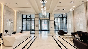 A modern hotel lobby with a reception desk, seating area, and large windows offering views of the street. - Upscale Studio Apartment Business Bay with Balcony and Free Parking by BelVilla (Dubai)