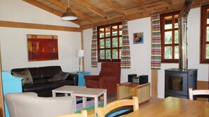 A cozy living room with a sofa, armchair, wooden table, and a wood-burning stove.