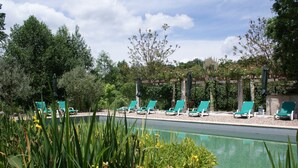 A pool area with green lounge chairs and a pergola with umbrellas.