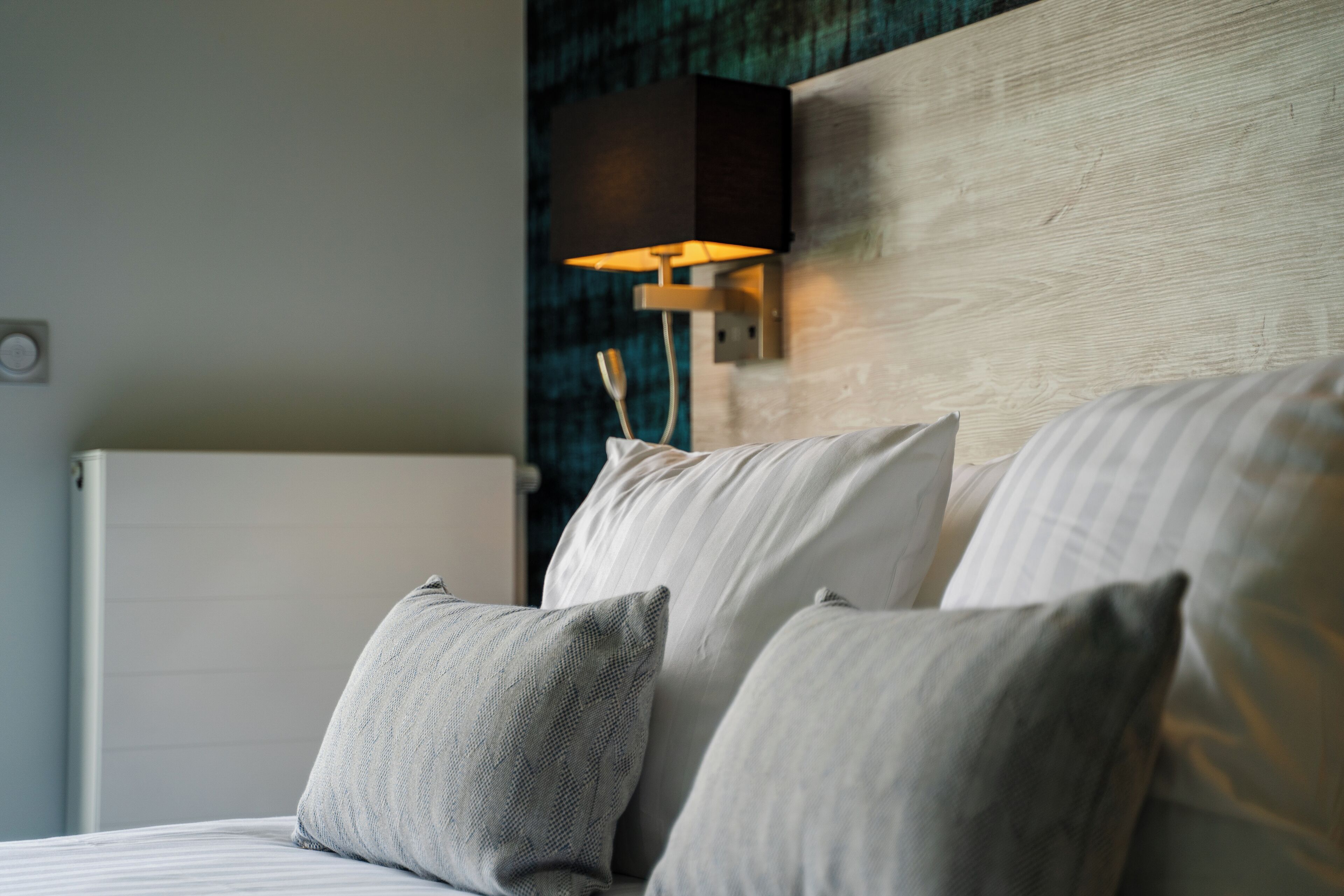 A neatly made bed with pillows and a wall-mounted lamp.