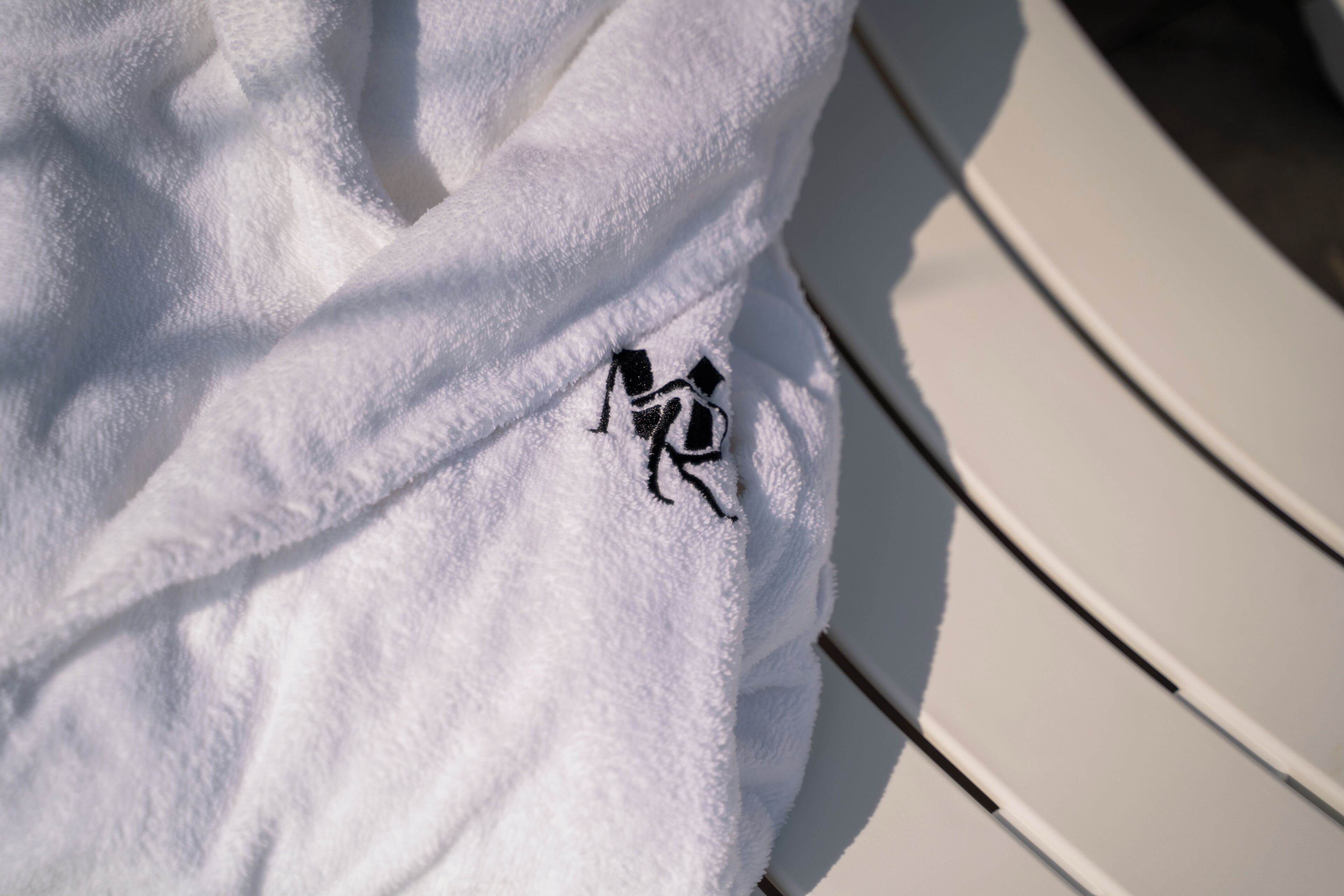 Une serviette blanche ornée d’un logo noir brodé, posée sur une chaise blanche.