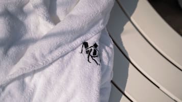 Une serviette blanche ornée d’un logo noir brodé, posée sur une chaise blanche.