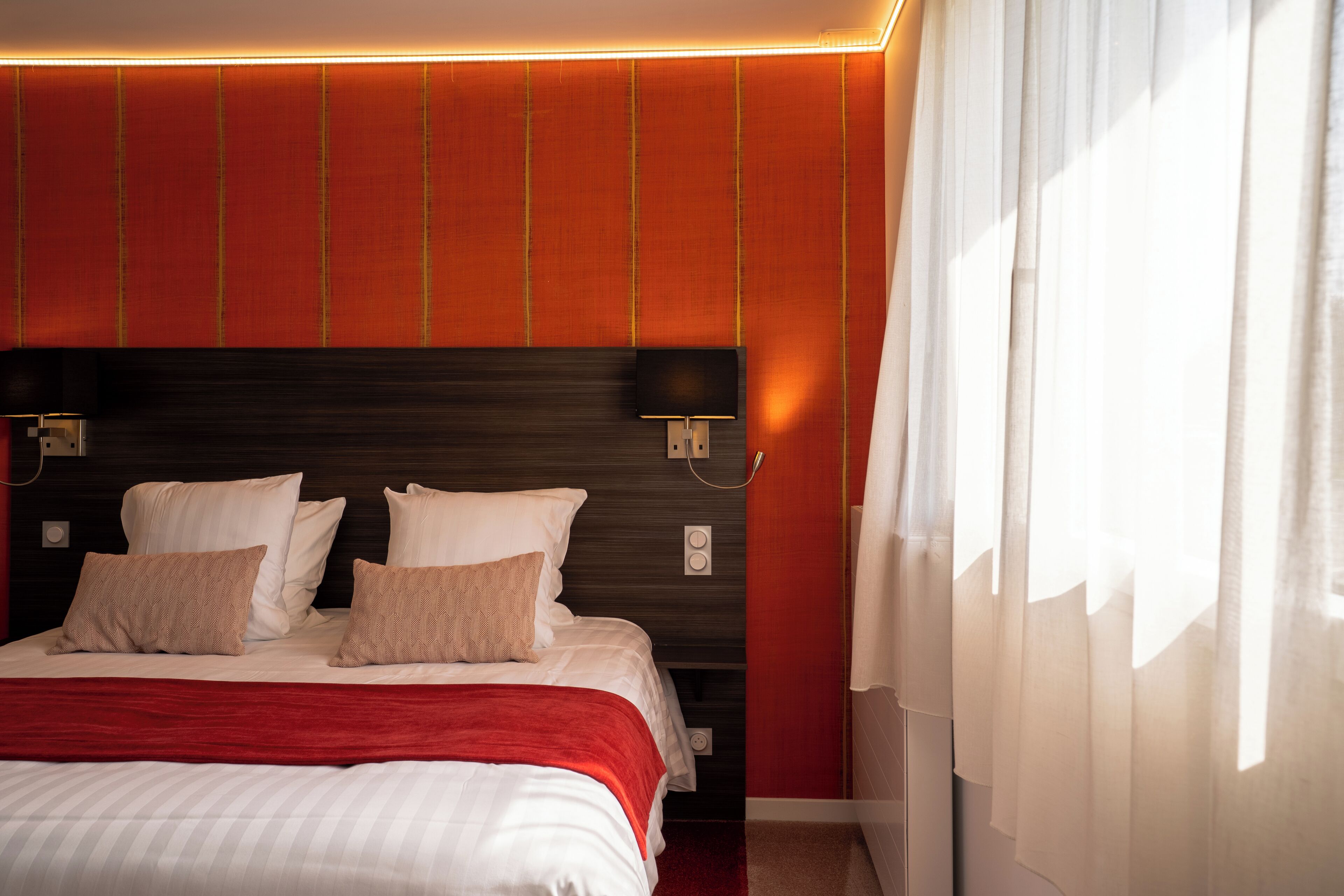 A hotel room with a large bed, a dark headboard, and a red accent wall.