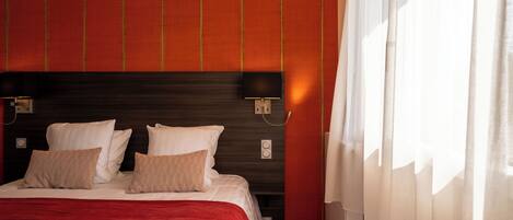 A hotel room with a large bed, a dark headboard, and a red accent wall.