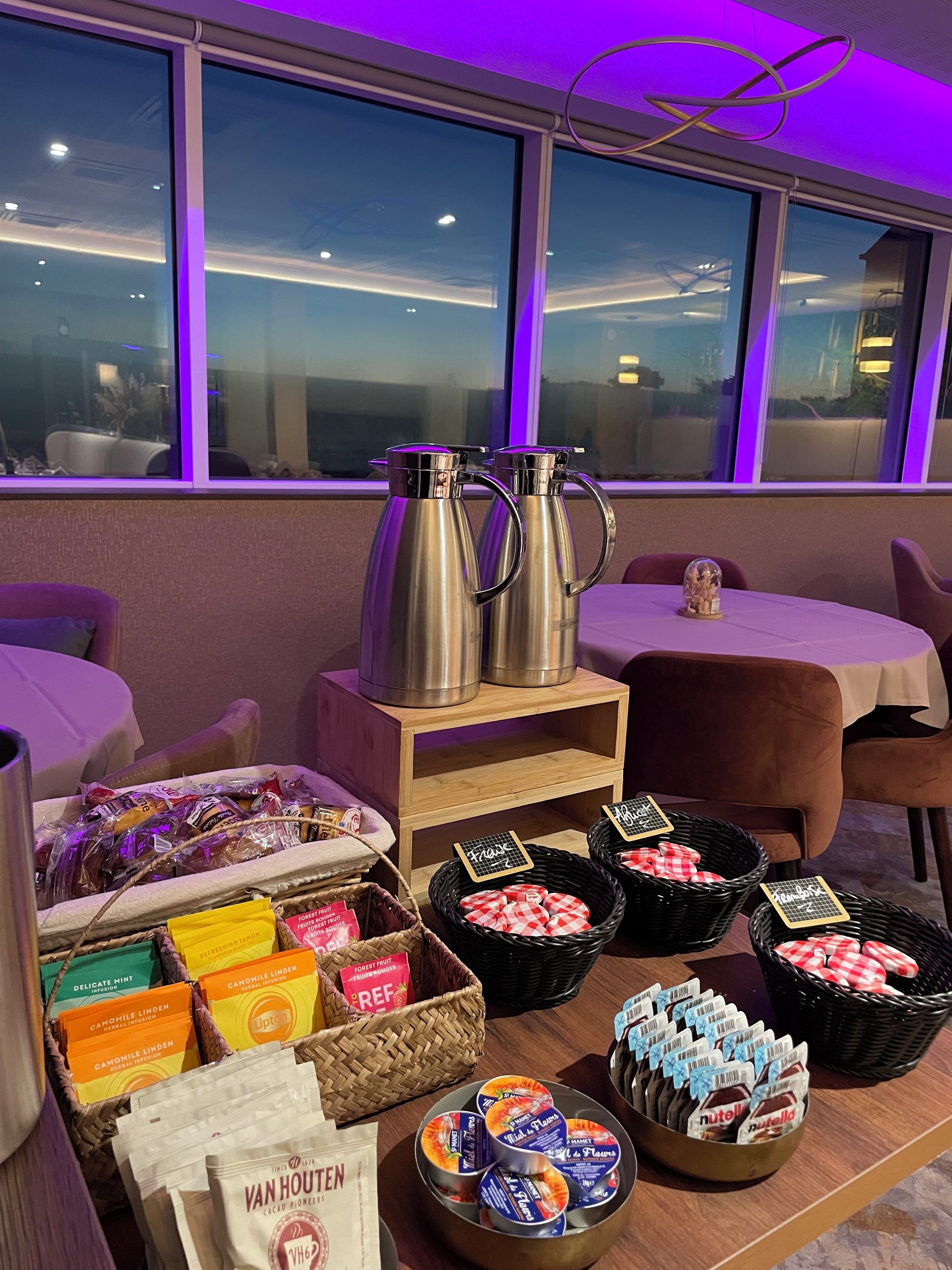 A breakfast buffet setup with coffee pots, baskets of pastries, and packaged goods.