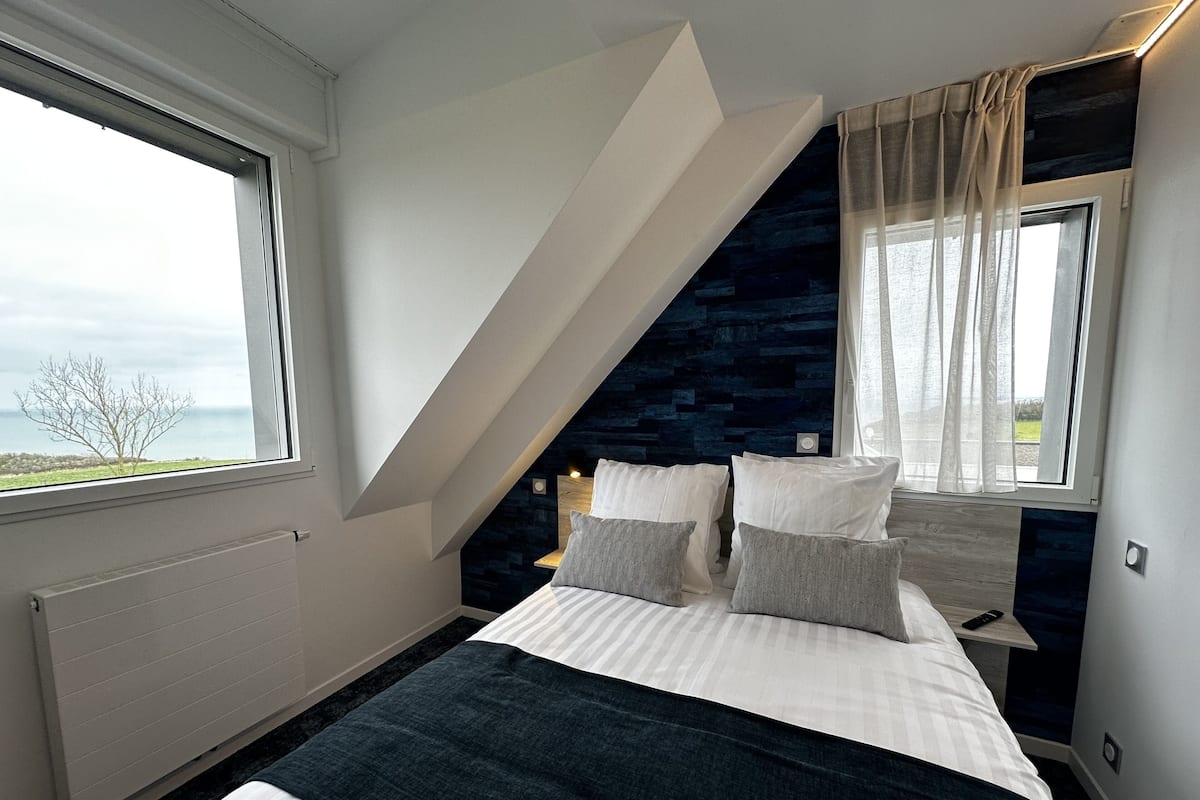 A bedroom with a bed, a window, a nightstand, and a view of the outdoors.