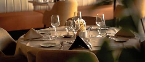 A restaurant setting with tables set for dining, including wine glasses, plates, and cutlery.