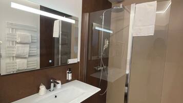 Un baño moderno con un lavamanos grande de color blanco, una ducha con cerramiento de vidrio y un espejo sobre el lavamanos.