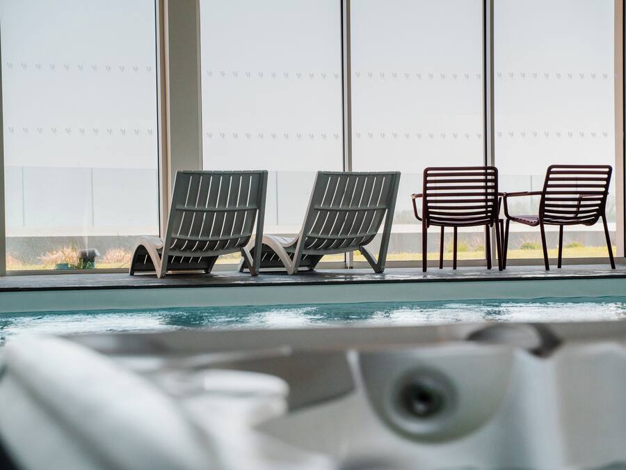 A poolside area with three lounge chairs and a view of the outdoors through large windows.
