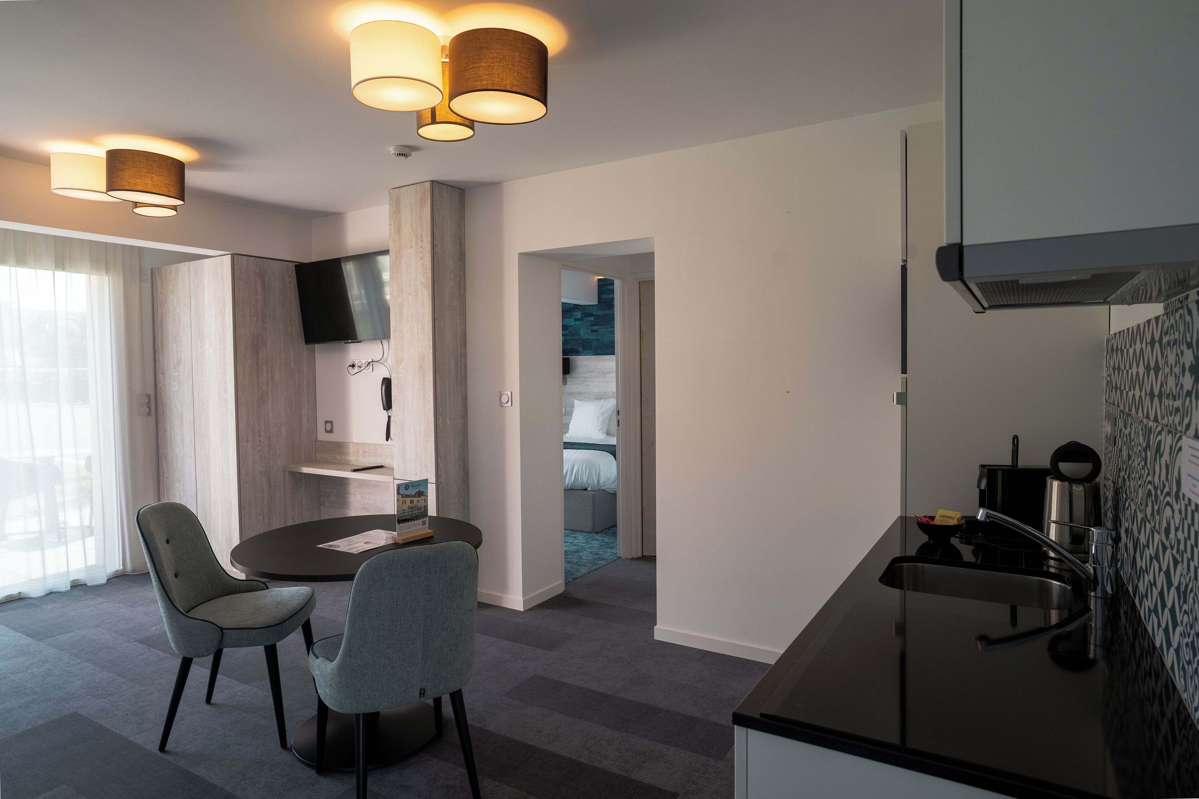 Moderni hotellihuone, jossa on ruokailutila, pieni keittiö ja näkymä siniselle ulkoalueelle.
