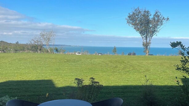 Un patio exterior con dos sillas y una mesa, con vista a un campo cubierto de césped y el mar.