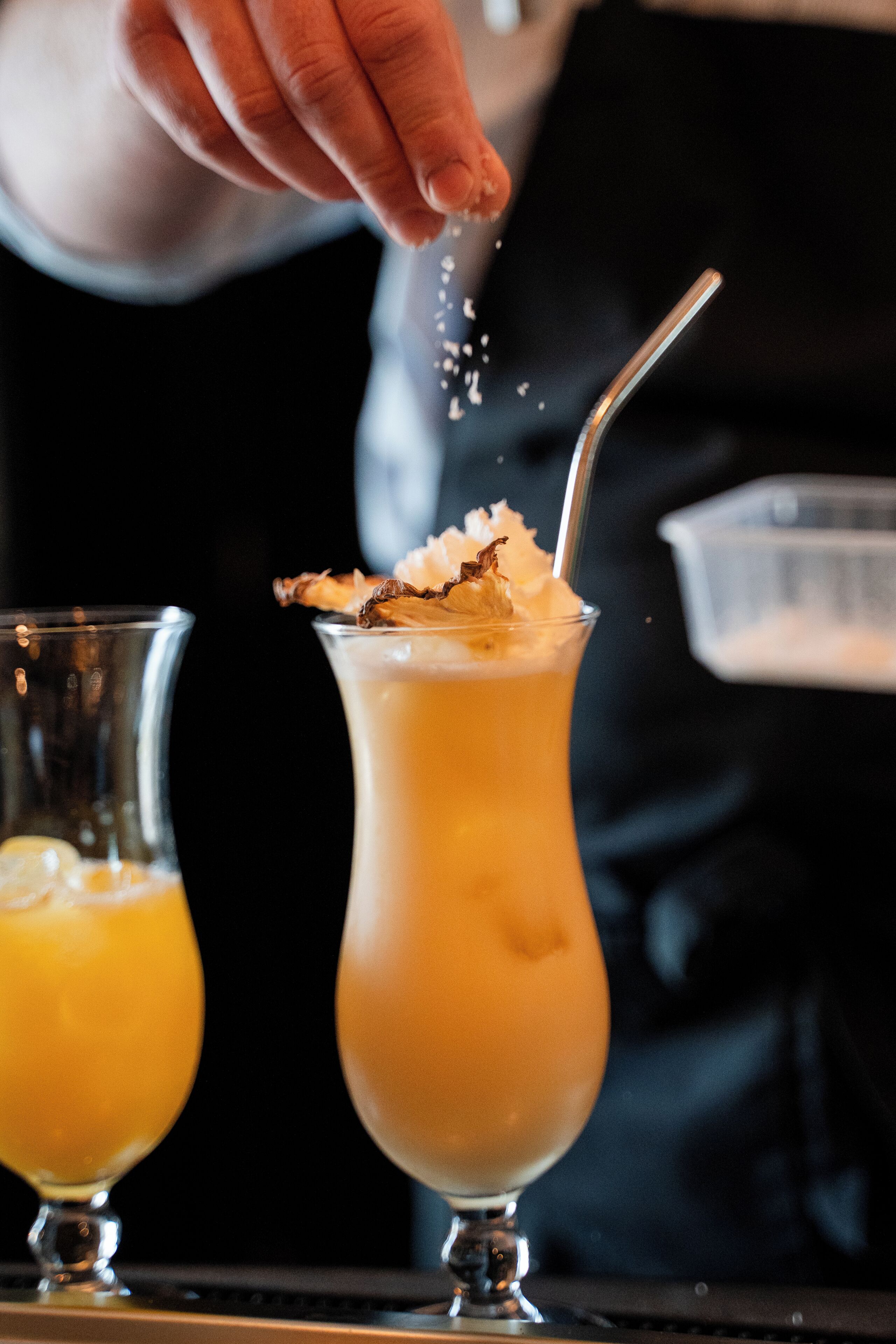 Um bartender preparando um cocktail, adicionando uma colher de açúcar.