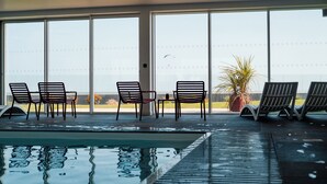 Una piscina interior con sillones de descanso y vistas al océano a través de amplios ventanales.