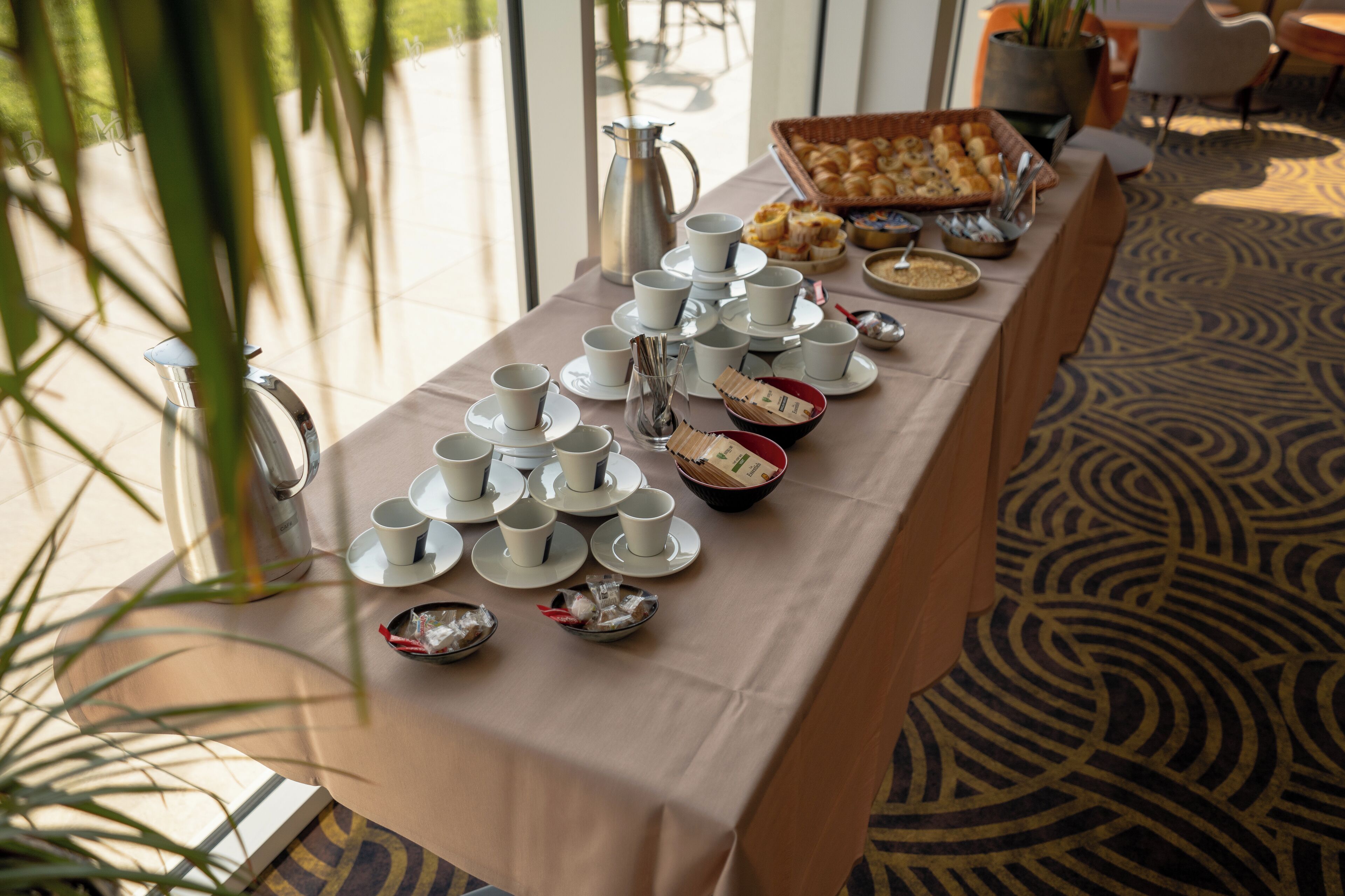 A breakfast buffet setup with multiple cups, plates, and a pitcher on a table.