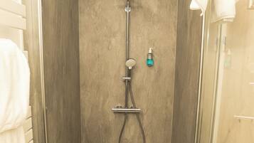 Una ducha a pie con puerta de cristal, un cabezal de ducha manual, un grifo de pared y una pequeña botella de champú.