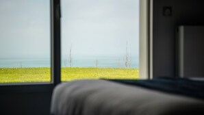 Una habitación con un amplio ventanal que da a un campo cubierto de hierba y una masa de agua.
