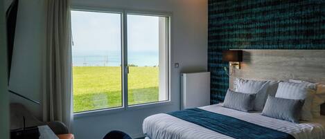A modern hotel room with a large bed, a desk with a chair, a view of the ocean, and a patterned wall.
