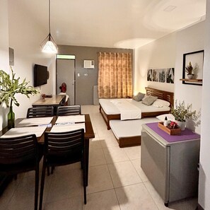 Habitación de hotel compacta con cama, escritorio, mesa de comedor con sillas y kitchenette.