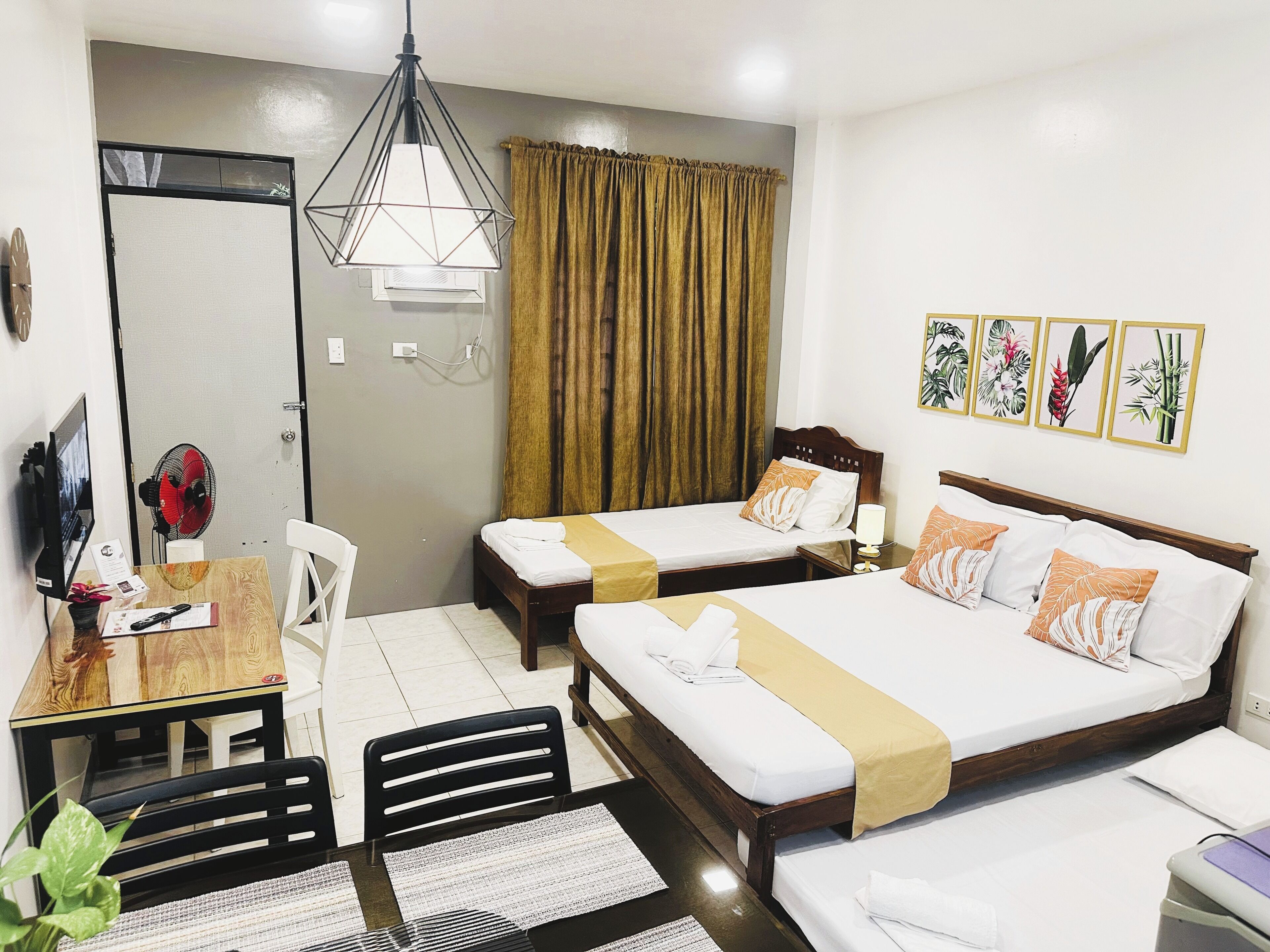 A hotel room with two beds, a desk with a chair, a dining table, and a large window with curtains.