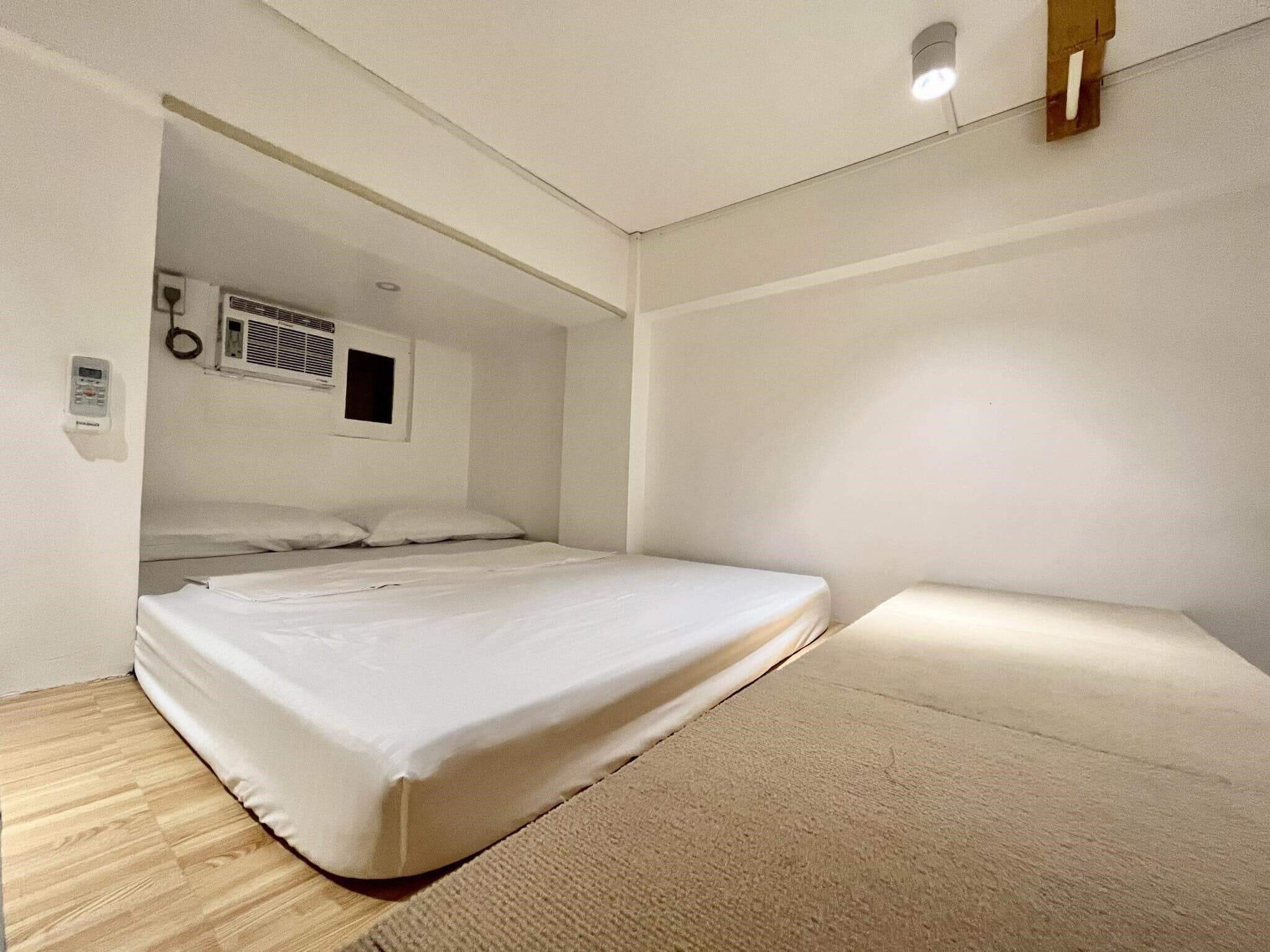A single bed in a room with a sloped ceiling, a wall-mounted air conditioning unit, and a small window.