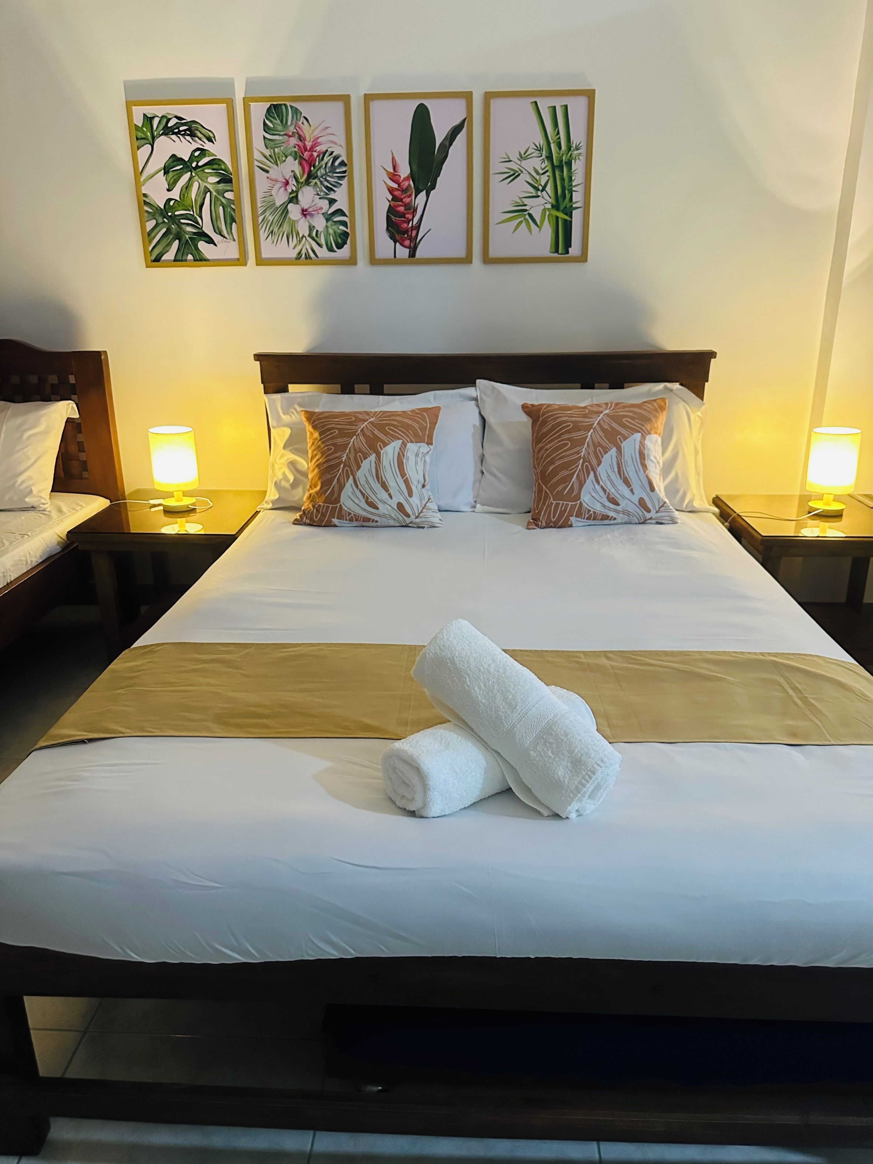 A hotel room with a large bed, two bedside tables with lamps, a headboard, and three framed botanical prints on the wall.