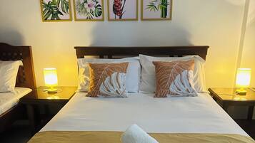 A hotel room with a large bed, two bedside tables with lamps, a headboard, and three framed botanical prints on the wall.