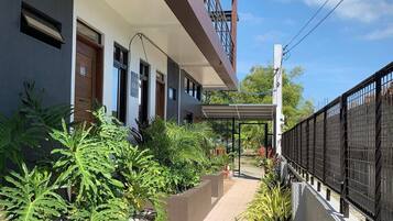 Un edificio moderno con un paseo techado, plantas en macetas y una valla metálica.