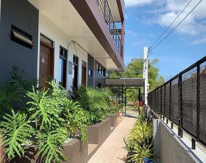 A modern building with a covered walkway, potted plants, and a metal fence. - Jora Residences (Dagupan)