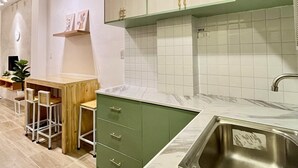 A modern kitchen with a marble countertop, green cabinets, and a stainless steel sink.