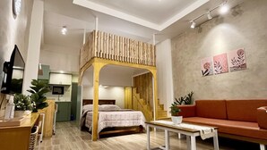 A modern bedroom with a wooden canopy bed, a red sofa, a small table, and a staircase leading to an upper level.