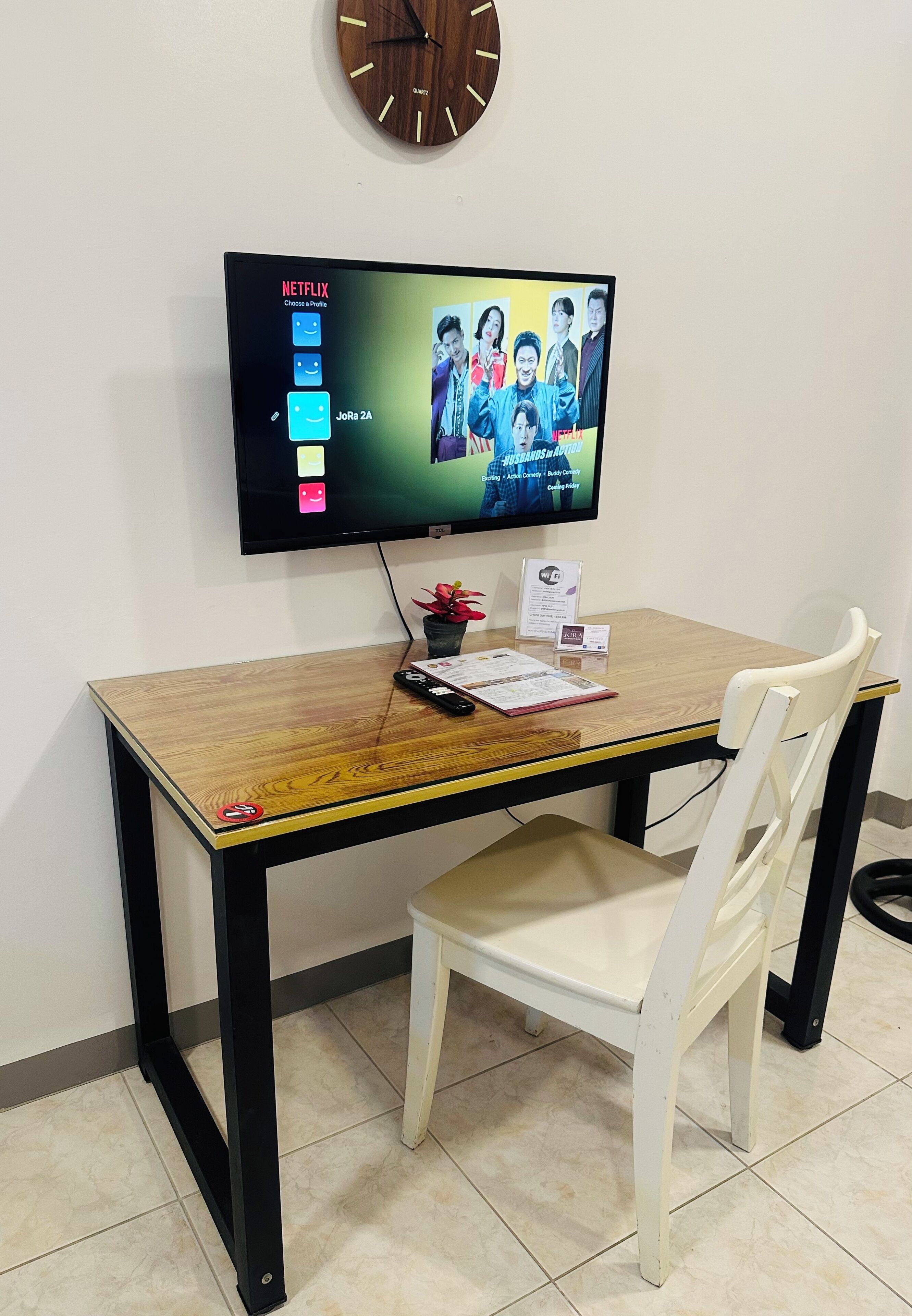 Una taula de fusta amb un televisor de pantalla plana muntat a la part superior, una cadira, un rellotge i alguns documents damunt la taula.