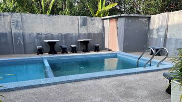 A rectangular pool with a blue edge, surrounded by a concrete deck. There are four small tables and a bench along the poolside.