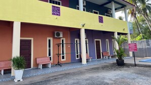 A multi-story building with a yellow and purple facade, air conditioning units, and a covered entrance area with benches and potted plants. - OYO 90967 Homestay Chalet Warisan Siti  (Langkawi)