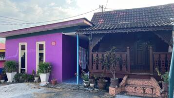 A two-story house with a purple exterior and a brown roof. There are potted plants and a staircase leading to the upper floor.