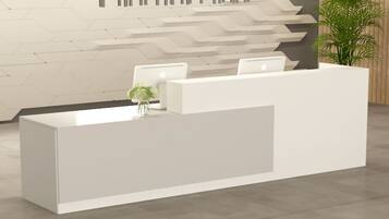 A reception desk with two chairs, a vase with flowers, and a plant to the right.