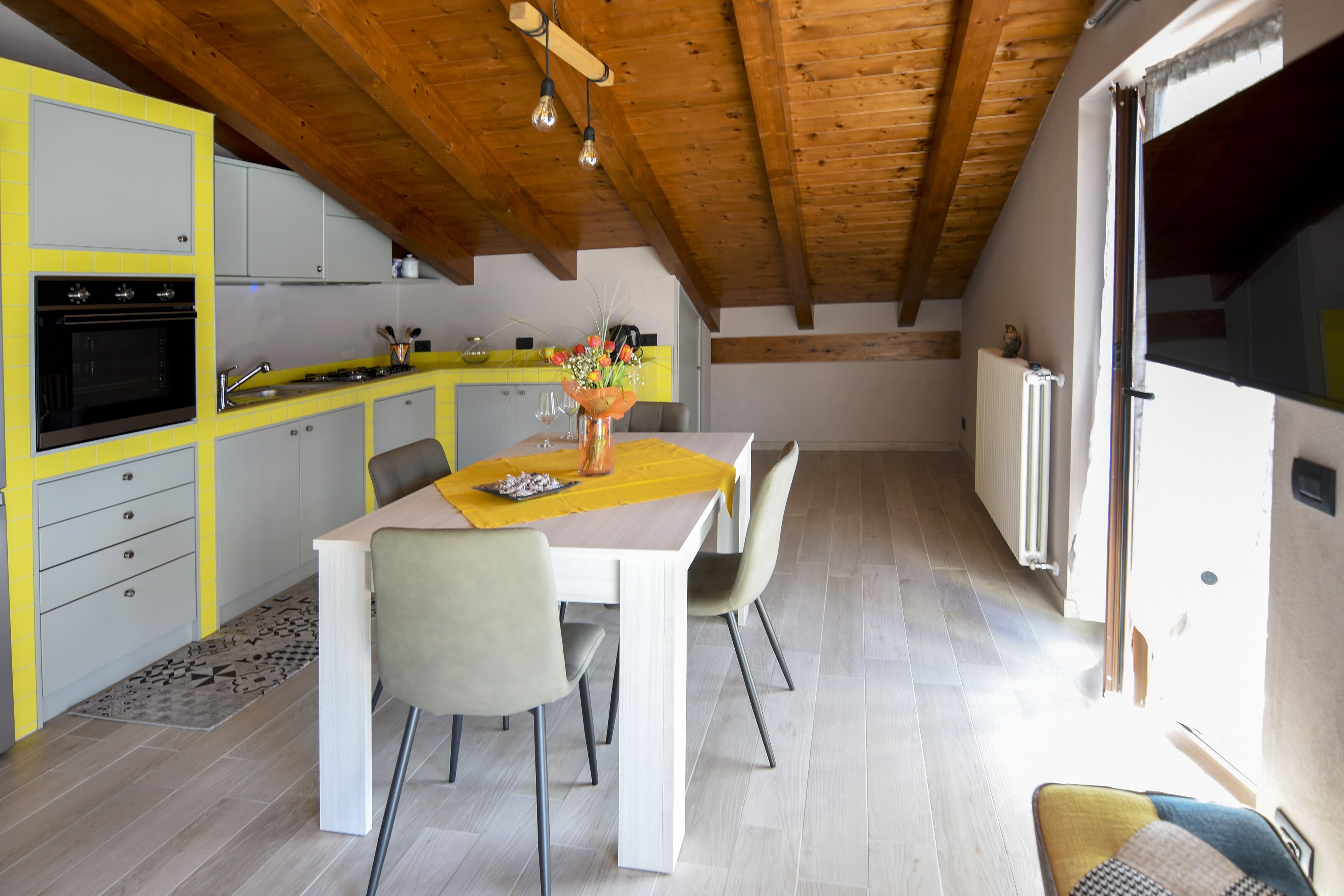 A modern kitchen with yellow cabinets, a dining area with a table and chairs, and a wooden ceiling.