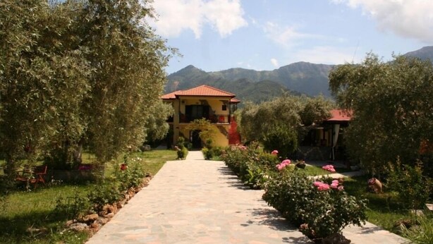 Un sentier mène à un bâtiment entouré d’une végétation luxuriante, avec des montagnes en arrière-plan.