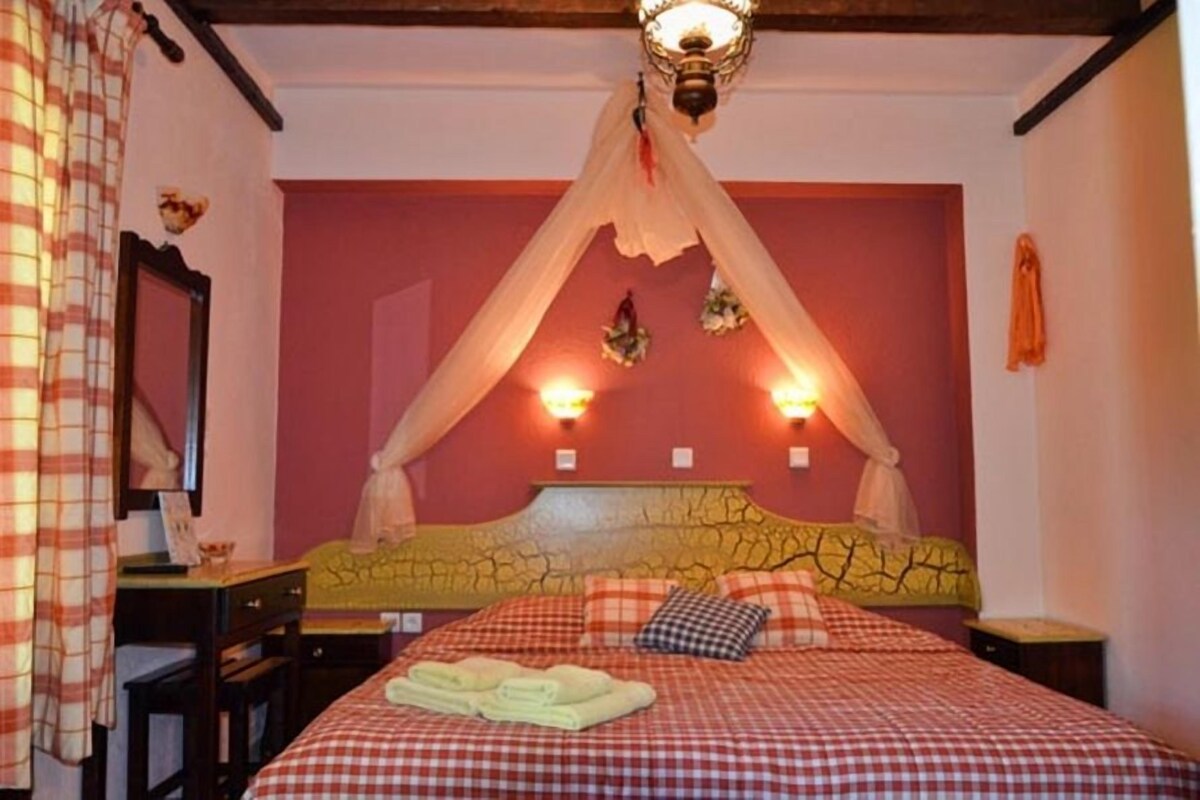 A bedroom with a bed under a canopy, a bedside table, a mirror, and a wall-mounted light fixture.