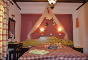 A bedroom with a canopy bed, a bedside table, a mirror, and a wall-mounted light fixture. - Maria Hotel (Thasos)