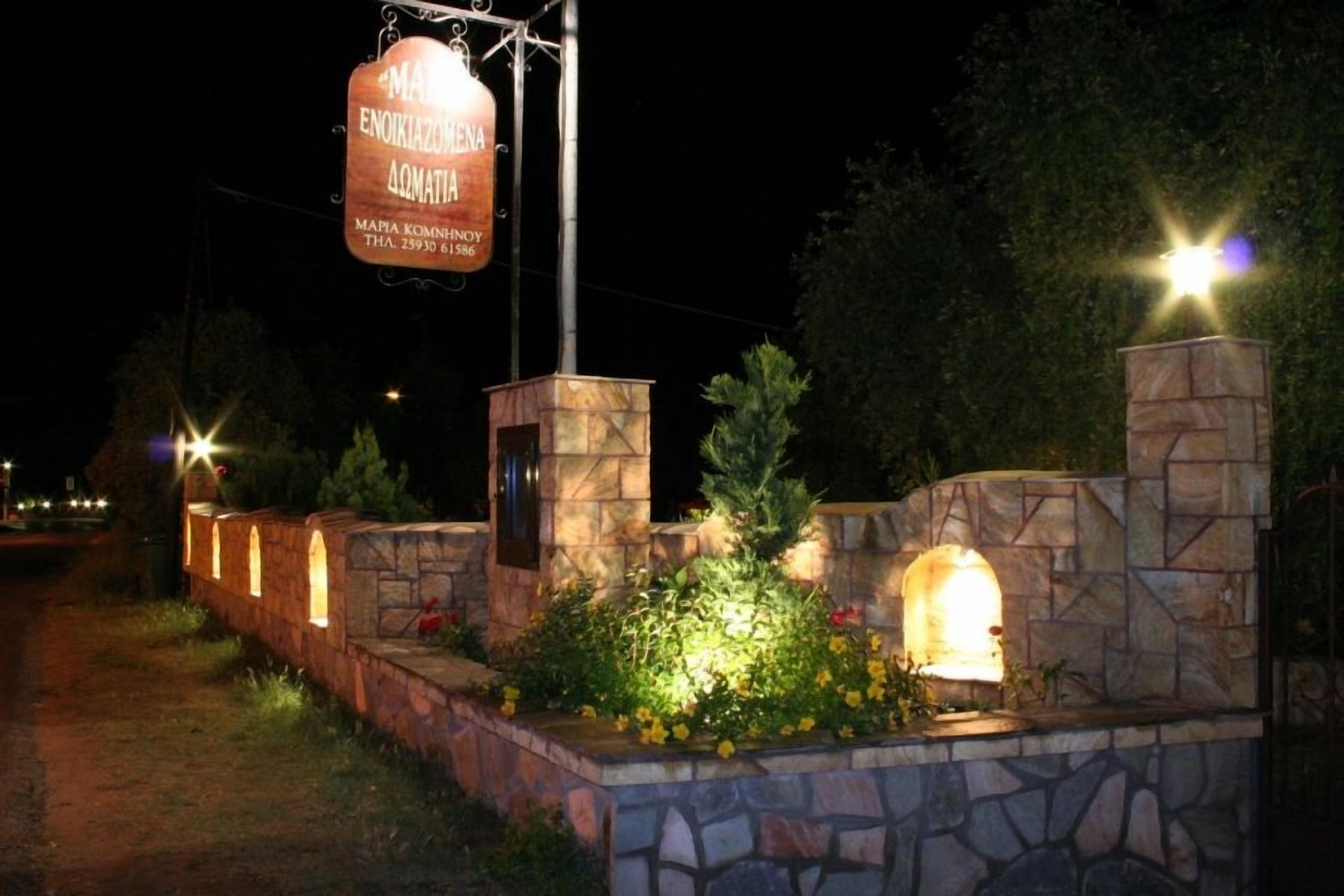 A stone wall with a sign for a restaurant, surrounded by greenery and illuminated by street lights.