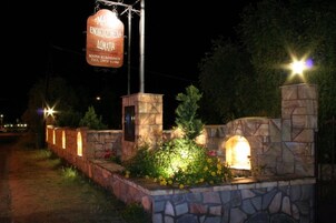Un muro de piedra con un letrero de restaurante, rodeado de follaje e iluminado por farolas.