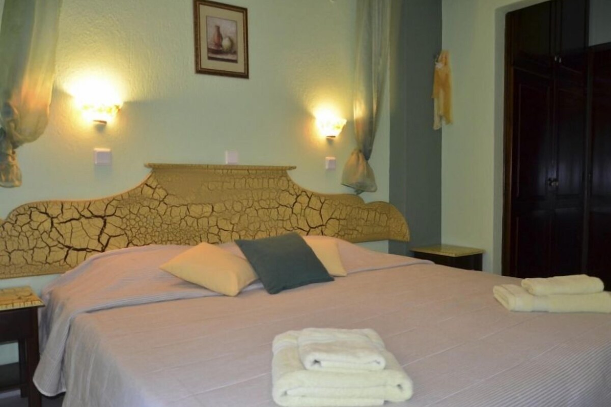 A hotel room with a large bed, two bedside lamps, a headboard with a cracked pattern, and a framed picture on the wall.
