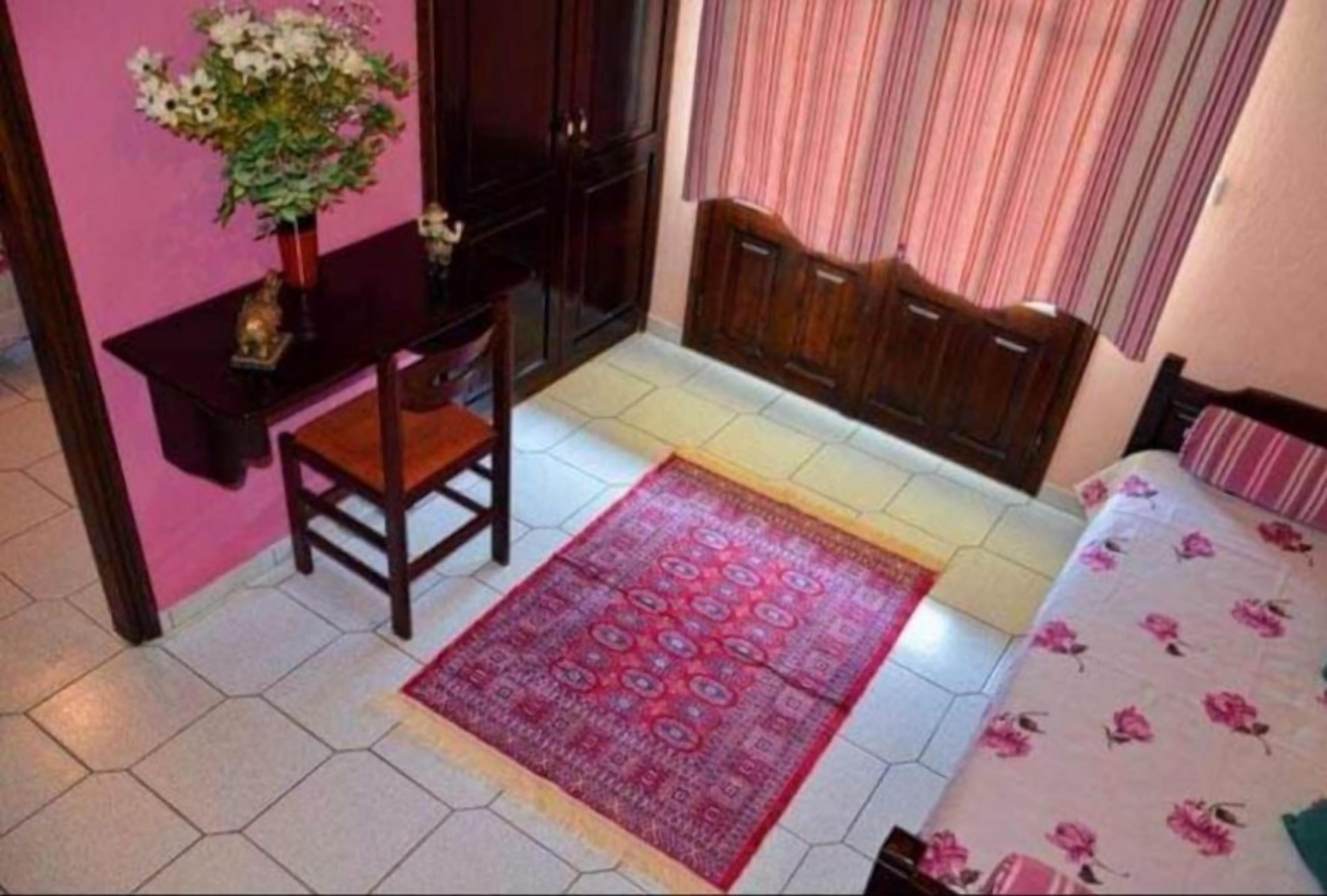 A bedroom with a bed, a chair, a desk, and a small table with a vase of flowers.