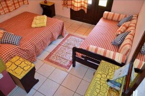 A room with two beds, each with checkered bedding and pillows, a small rug, and a yellow table with a remote control. - Maria Hotel (Thasos)