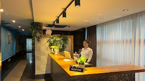 A reception desk with a sign reading "RECEPTION," a plant, and a person standing behind it. - INNO CONCEPT HOTEL (Antalya)