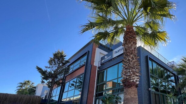 A modern building with a glass facade, a sign for 'huntas' and 'MNP Concert', and a palm tree in the foreground. - INNO CONCEPT HOTEL (Antalya)