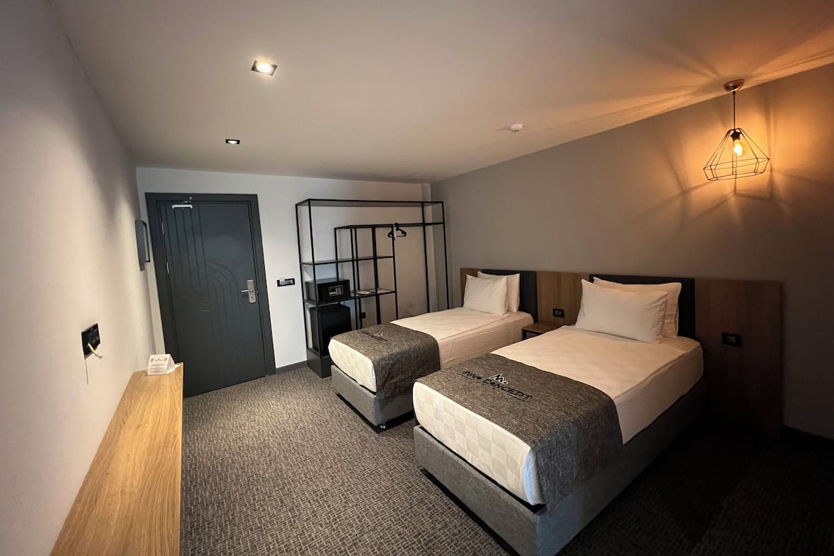 A hotel room with two beds, a desk, a wardrobe, and a ceiling light.
