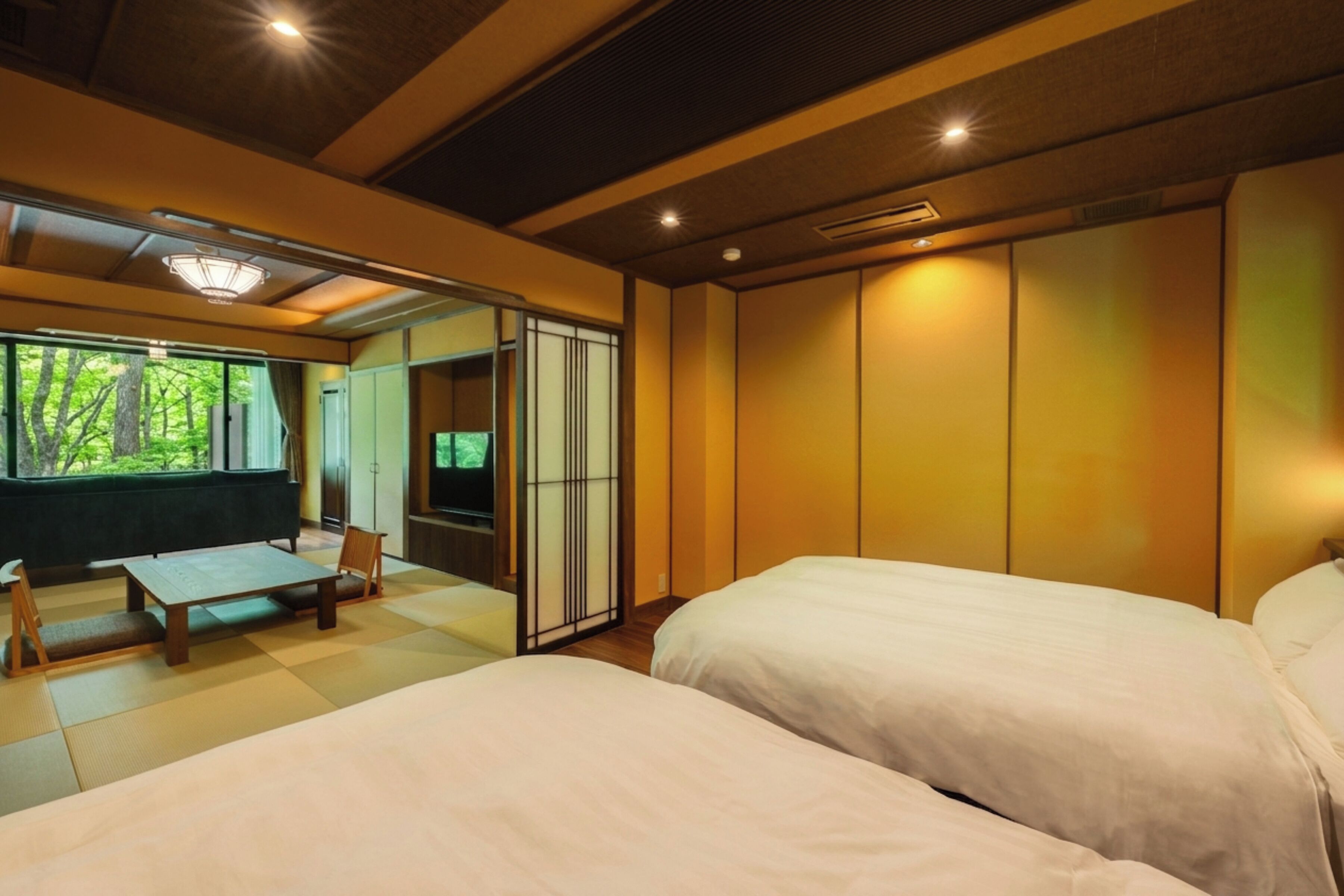A room with two beds, a wooden table, and a sliding door leading to a balcony.